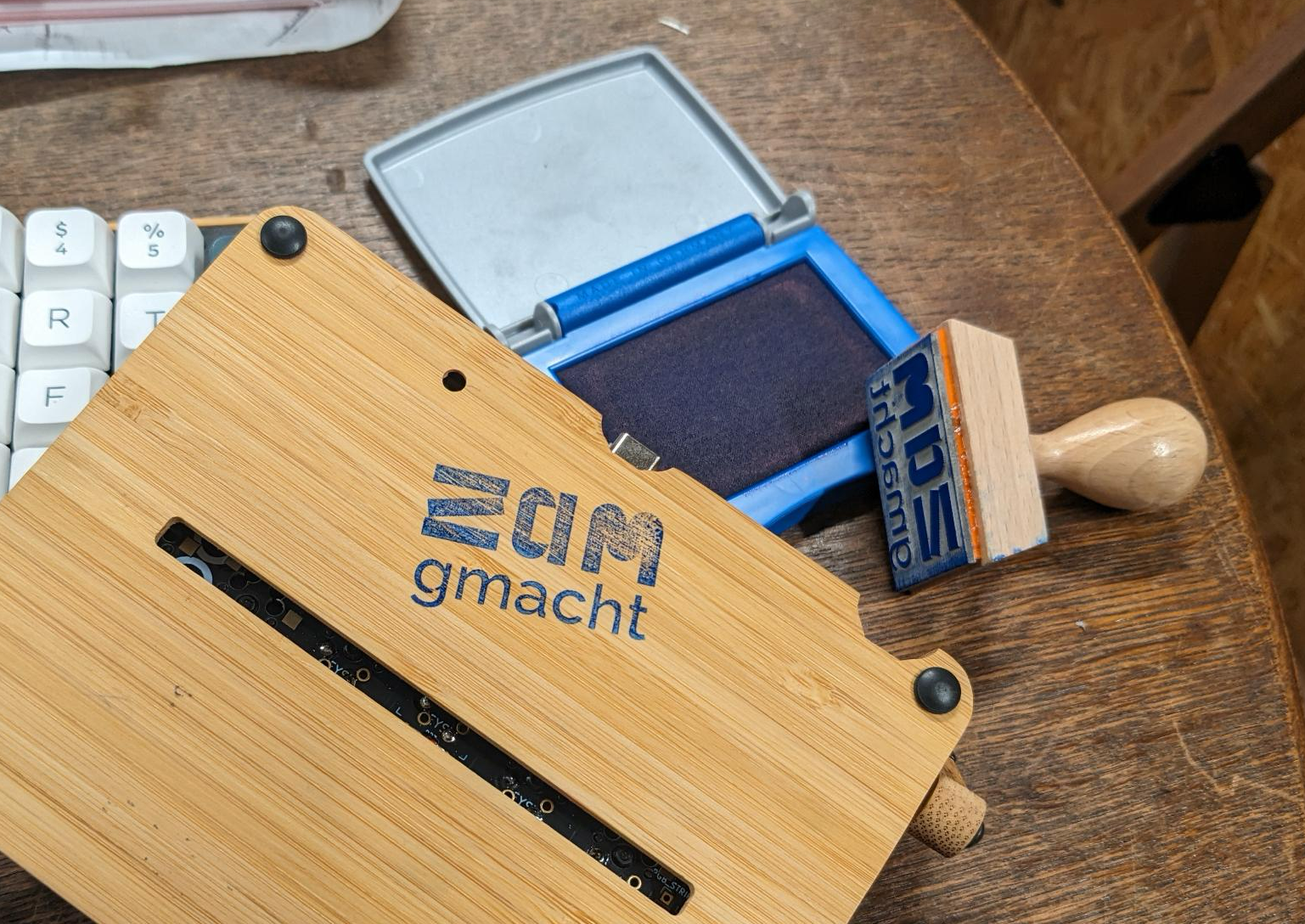 Es ist ein Stempel, Stempelkissen und ein Holz mit Stempelabdruck "ZAMgemacht" zu sehen.